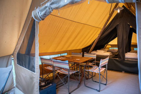 Binnenkant van een safaritent met houten tafel, stoelen en comfortabele slaapplaatsen gereed.