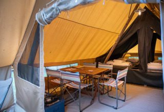 Intérieur d'une tente safari avec table à manger en bois, chaises rayées et lits confortables prêts.