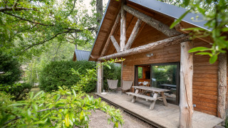 Blockhütte mit überdachter Veranda und Picknicktisch, umgeben von Bäumen im Huttopia Rambouillet, Frankreich.