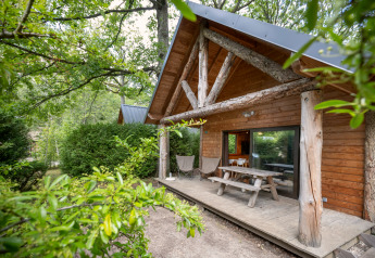 Houten blokhut met overdekte veranda, picknicktafel en bosrijke omgeving bij Huttopia Rambouillet in Frankrijk.