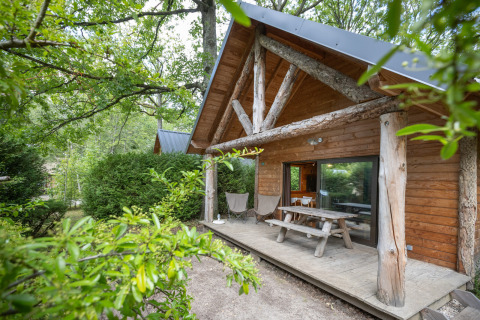 Houten hut met overdekt terras, picknickbank en groene omgeving bij Huttopia Rambouillet in Frankrijk.