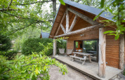 Blockhütte mit überdachter Veranda und Picknicktisch, umgeben von Bäumen im Huttopia Rambouillet, Frankreich.