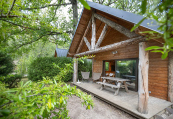 Blockhütte mit überdachter Veranda und Picknicktisch, umgeben von Bäumen im Huttopia Rambouillet, Frankreich.