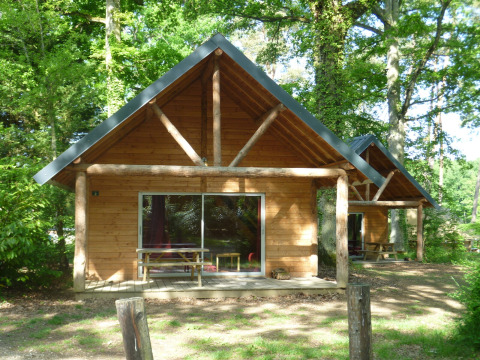 Cabaña de madera en Huttopia Rambouillet, Francia, rodeada de árboles y naturaleza verde.