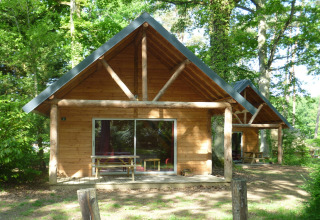 Cabaña de madera en Huttopia Rambouillet, Francia, rodeada de árboles y naturaleza verde.