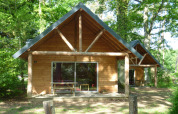 Wooden cabin at Huttopia Rambouillet in France, nestled among lush green trees with a porch.