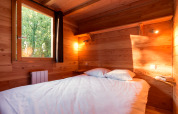 Chambre douillette dans une cabane en bois avec lit double, étagère et lumière naturelle de la fenêtre.