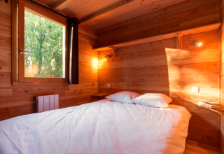 Slaapkamer in een gezellige houten chalet met tweepersoonsbed, boekenplank en veel natuurlijk licht.