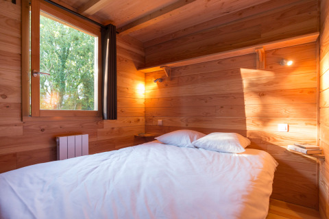 Gemütliches Schlafzimmer in einer Holzhütte mit Doppelbett, großem Fenster und Blick ins Grüne.