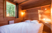 Acogedor dormitorio de cabaña con paredes de madera, cama doble, estantería y ventana al exterior.