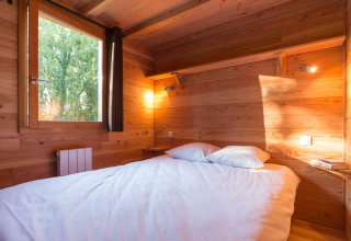 Acogedor dormitorio de cabaña con paredes de madera, cama doble, estantería y ventana al exterior.