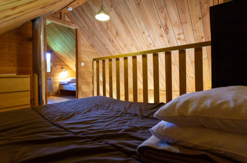 Dachzimmer mit Holzverkleidung in The cabin at Huttopia Rambouillet, Frankreich, vom Bett aus gesehen.