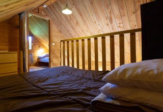Loftsoveværelse med træinteriør i The cabin at Huttopia Rambouillet, Frankrig, set over sengen.
