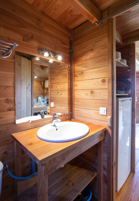 Salle de bain en bois dans The cabin à Huttopia Rambouillet, France, avec lavabo et miroir visibles.