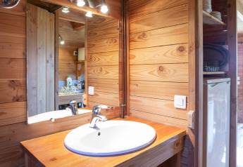 Salle de bain en bois dans The cabin à Huttopia Rambouillet, France, avec lavabo et miroir visibles.