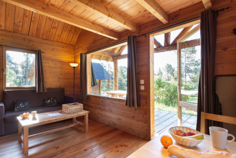 Knusse houten chalet bij Huttopia Rambouillet in Frankrijk met zicht op de natuur door grote ramen.