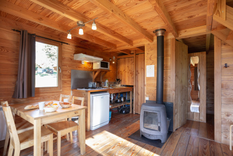 Interior acogedor de cabaña con mesa de comedor, estufa y cocina en Huttopia Rambouillet, Francia.