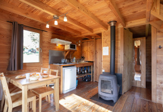 Interior acogedor de cabaña con mesa de comedor, estufa y cocina en Huttopia Rambouillet, Francia.