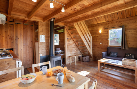 Interiør af træhytte på Huttopia Rambouillet, Frankrig, med spisebord, stue og trappe til hems.