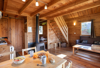 Acogedor interior de cabaña de madera en Huttopia Rambouillet, Francia, con comedor y escalera al altillo.