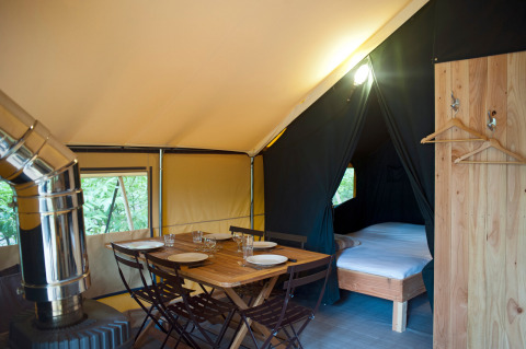Interior de una tienda safari con mesa de comedor, estufa y cama en Huttopia Rambouillet, Francia.