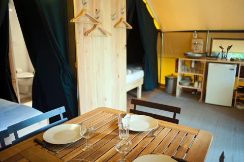 Interior de la tienda safari Tente Trappeur en Huttopia Rambouillet, Francia, con comedor y cocina pequeña.