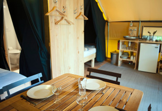 Interior de la tienda safari Tente Trappeur en Huttopia Rambouillet, Francia, con comedor y cocina pequeña.
