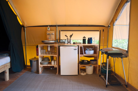 Safari tent interior with a kitchenette setup including fridge, sink, stove, and kitchen utensils.