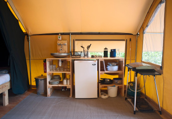 Interno di tenda safari con angolo cucina: frigorifero, lavandino, fornello e utensili da cucina.