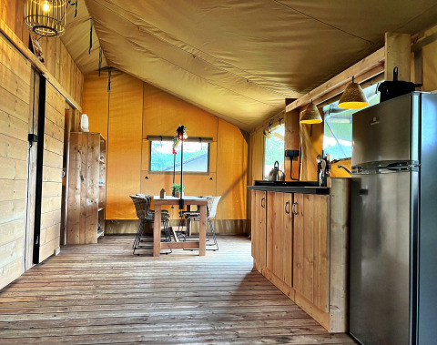 Interior de una tienda glamping con suelo de madera, cocina y mesa en Per Amore del Vino, Italia.