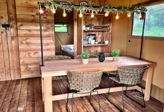 Zona de comedor interior en tienda glamping en Per Amore del Vino, Italia, con mesa de madera y luces.