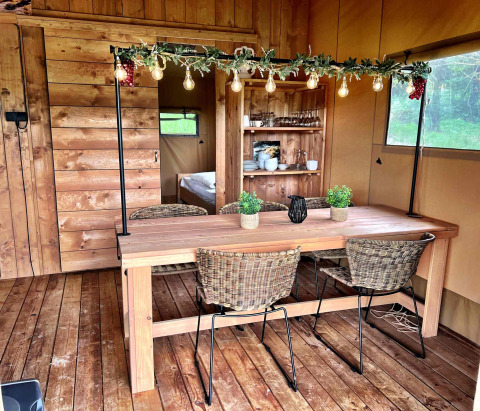 Zona de comedor interior en tienda glamping en Per Amore del Vino, Italia, con mesa de madera y luces.