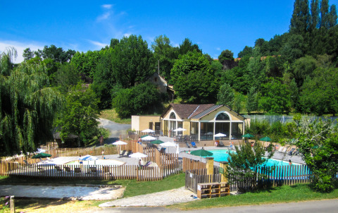 Piscina y casa de vacaciones entre árboles en Huttopia Sarlat, parque de vacaciones en Nouvelle-Aquitaine, Francia.