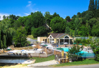 Zwembad en huisje tussen groen bij Huttopia Sarlat, een vakantiepark in Nouvelle-Aquitaine, Frankrijk.