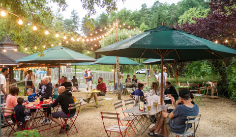 Ambiente de comida al aire libre en Huttopia Sarlat, parque vacacional en Nouvelle-Aquitaine, Francia, con luces y sombrillas.