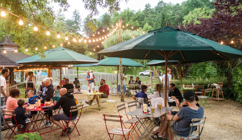 Ambiance de restauration en plein air au Huttopia Sarlat, parc de vacances en Nouvelle-Aquitaine, France, sous guirlandes lumineuses.