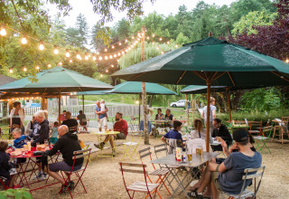 Ambiente de comida al aire libre en Huttopia Sarlat, parque vacacional en Nouvelle-Aquitaine, Francia, con luces y sombrillas.