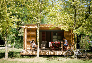 Twee personen genieten van een pauze bij een houten chalet tussen bomen in Huttopia Sarlat, Nouvelle-Aquitaine, Frankrijk.