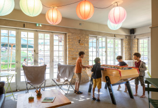 Kinder spielen Tischfußball in einem hellen Aufenthaltsraum mit Lampions bei Huttopia Sarlat in Frankreich.