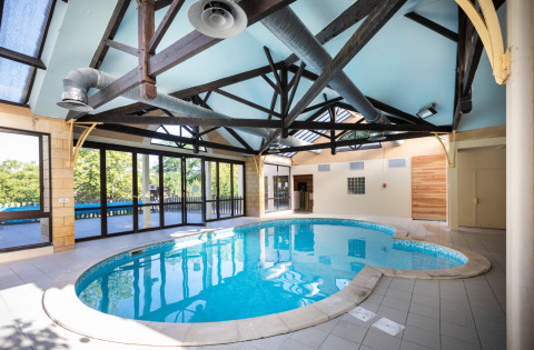 Piscine intérieure avec murs vitrés et poutres apparentes à Huttopia Sarlat en Nouvelle-Aquitaine, France.