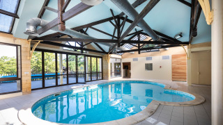 Piscina cubierta con paneles de vidrio y vigas de madera en Huttopia Sarlat, Nouvelle-Aquitaine, Francia.
