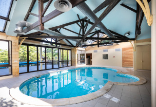Indoor swimming pool with glass walls and exposed beams at Huttopia Sarlat holiday park in France.