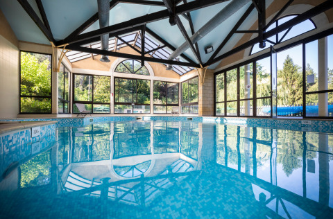 Piscina cubierta con paredes de vidrio y vistas al bosque en el parque vacacional Huttopia Sarlat, Francia.