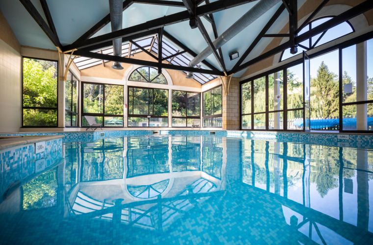 Indoor swimming pool with glass walls and forest views at Huttopia Sarlat holiday park in France.