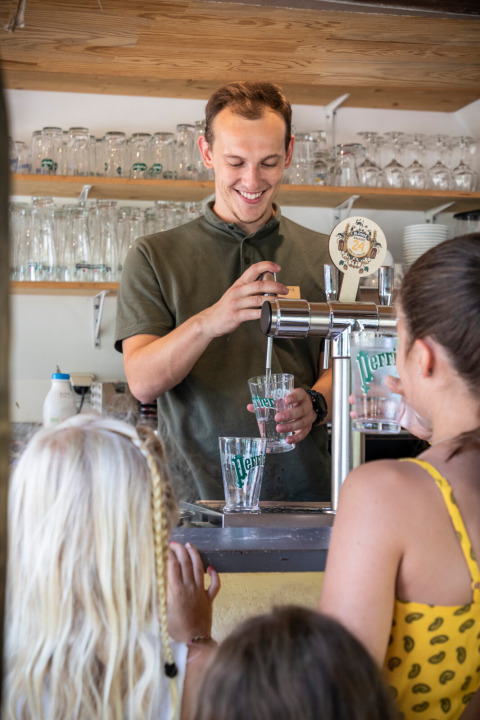 Un hombre sirve bebidas a los huéspedes en un bar en el parque vacacional Huttopia Sarlat en Nouvelle-Aquitaine, Francia.