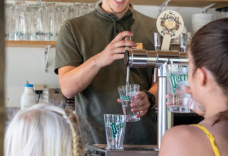 En mand skænker drikkevarer til gæster i en bar ved Huttopia Sarlat feriepark i Nouvelle-Aquitaine, Frankrig.