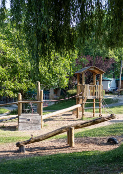 Parque infantil de madera rodeado de vegetación en Huttopia Sarlat, Nouvelle-Aquitaine, Francia.