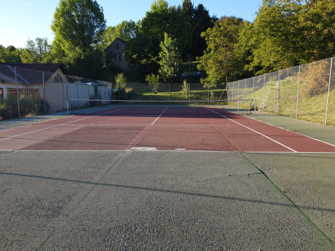Pista de tenis en Huttopia Sarlat, parque vacacional en Nouvelle-Aquitaine, Francia, rodeada de vegetación.