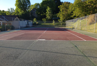 Tennisbane ved Huttopia Sarlat feriepark i Nouvelle-Aquitaine, Frankrig, omgivet af natur og bygninger.