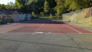 Pista de tenis en Huttopia Sarlat, parque vacacional en Nouvelle-Aquitaine, Francia, rodeada de vegetación.